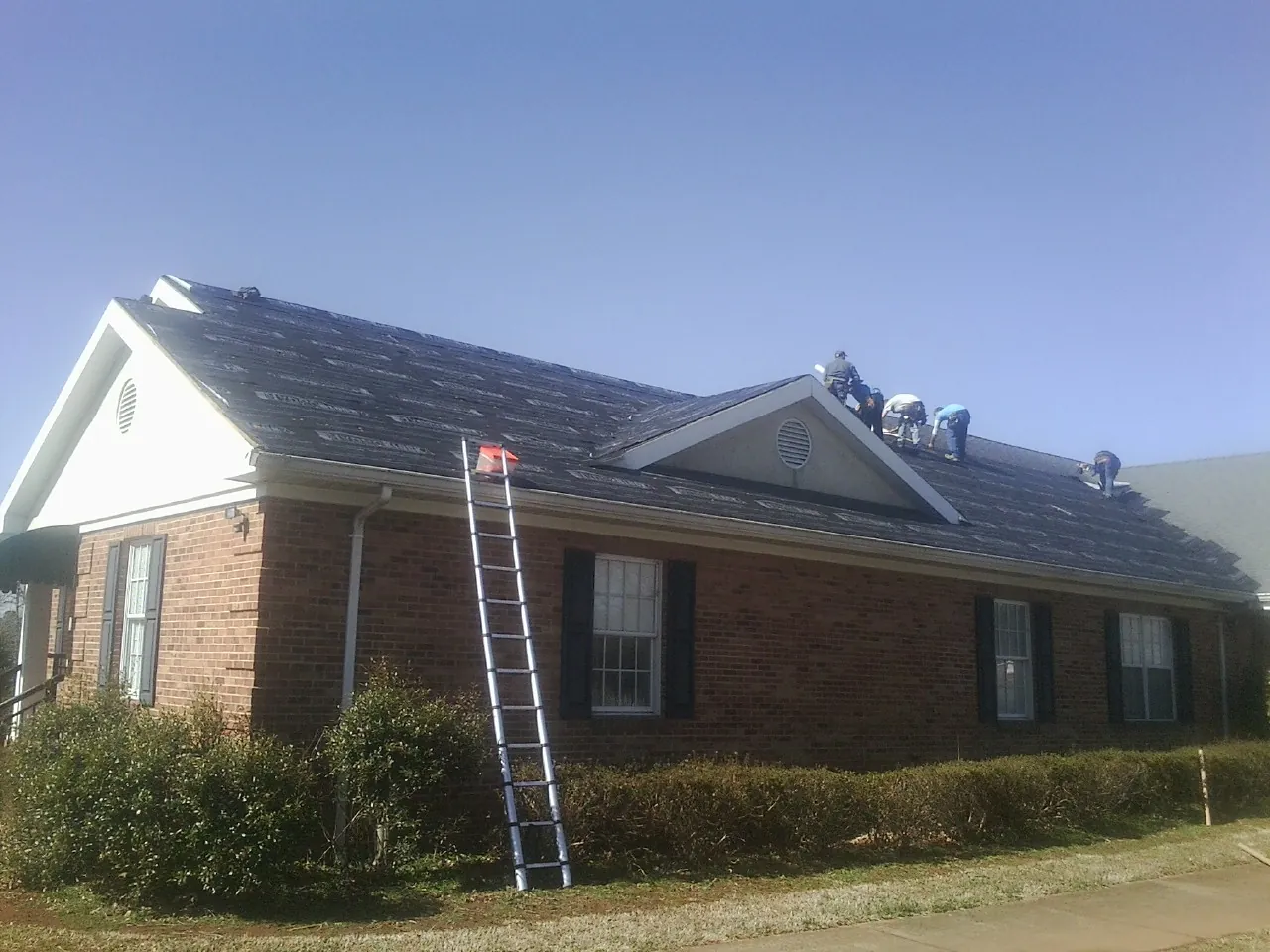 Crew tearing shingles off a brick ranch roof with a ladder set — Metal Roof Repair work by our crew in Livingston